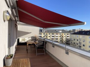Red electric sun blind on a roof terrace in a furnished apartment in Munich Laim